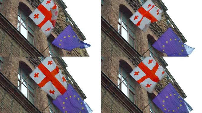 在一个阳光明媚的日子里，欧洲和格鲁吉亚的旗帜在风中飘扬，背景是建筑和天空