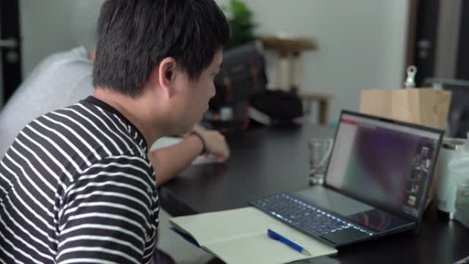 Man在家工作时与同事进行视频会议时会做笔记。