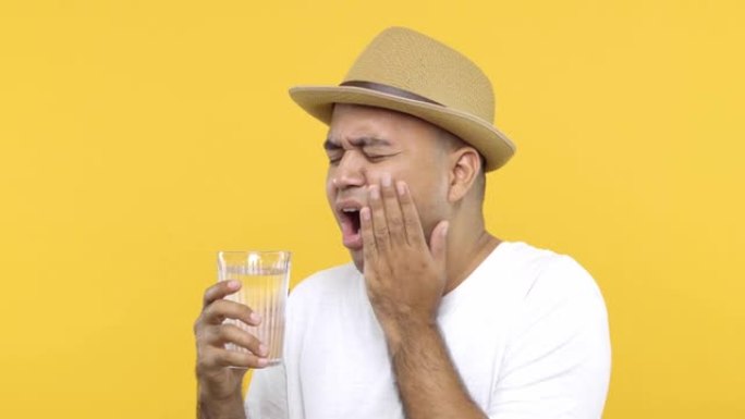 一个穿白衬衫的男人正在喝冷水。他敏感，牙齿酸痛，龋齿，讨厌，必须立即去看牙医。在黄色背景上。4k分辨