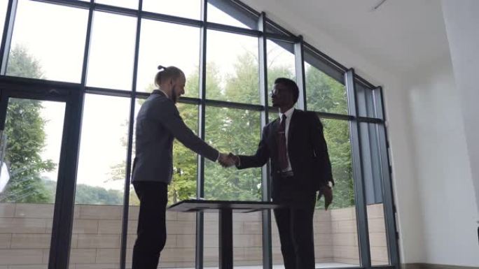 两个自信的商人，非洲裔美国人和高加索人在一次会议上握手，并在办公室签署了成功的商业合同。商业、成功、