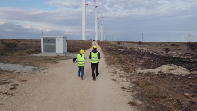 可再生能源系统。在风力涡轮机电站附近的野外工作的电力维护工程师的鸟瞰图，背后是喜怒无常的天空。两位同