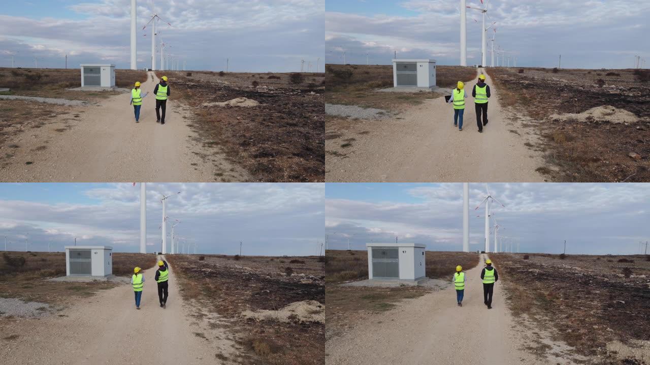 可再生能源系统。在风力涡轮机电站附近的野外工作的电力维护工程师的鸟瞰图，背后是喜怒无常的天空。两位同