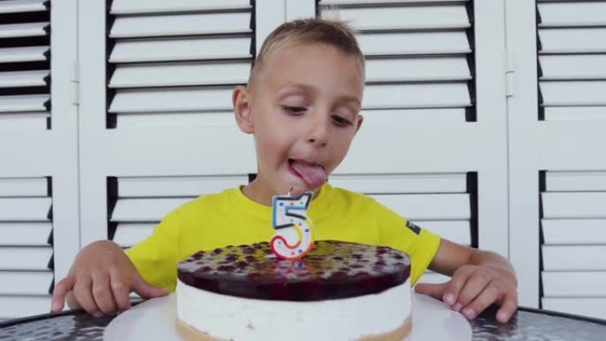 这个可爱的男孩正在庆祝他的5岁生日，坐在餐桌旁，端着一个美味的蛋糕，孤立在白色背景上。一个小男孩生日