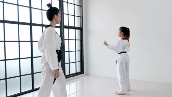 跆拳道教练在带玻璃窗的健身房中使用踢脚板或训练工具对受训者进行训练。学员腰带和背部的文字显示意味着跆