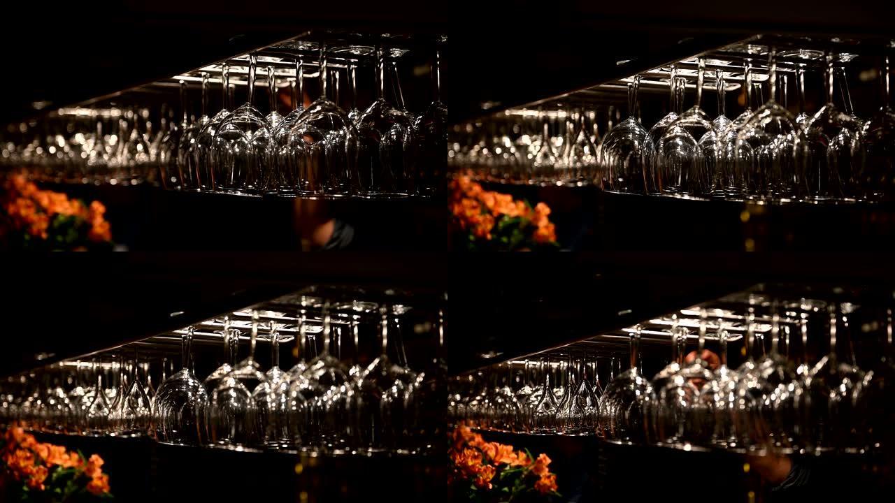 干净的酒杯倒挂在餐厅的酒吧架上方。酒保擦拭眼镜