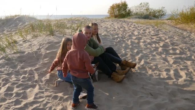 带着儿子和女儿以及一条狗的家庭坐在沙滩上