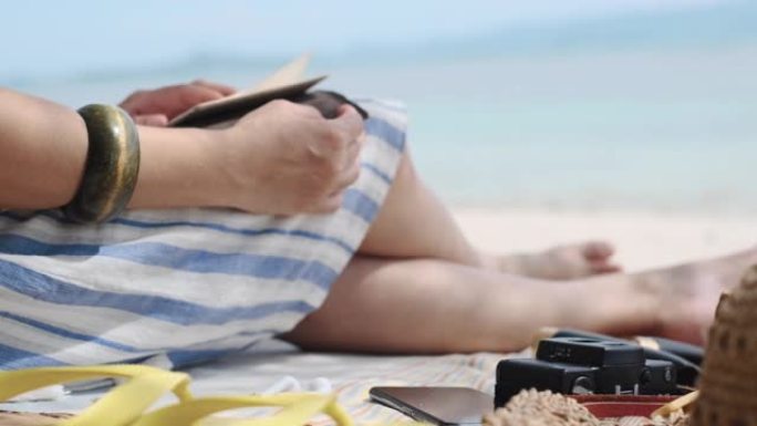 关闭女人在笔记本上计划新年目标，并在暑假期间使用耳机在海滩上听mucis
