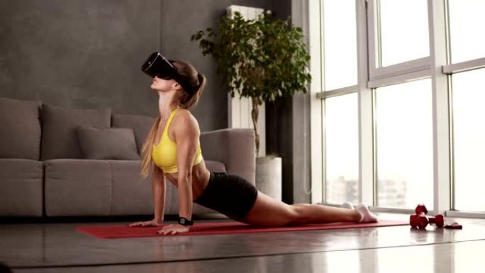 瑜伽女在家做晨练，在红色垫子上伸展，戴着虚拟现实面具。灵活的女孩练习vinyasa瑜伽surya n