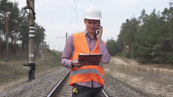 一名铁路工程师站在铁轨上，通过电话与上级进行了交谈。