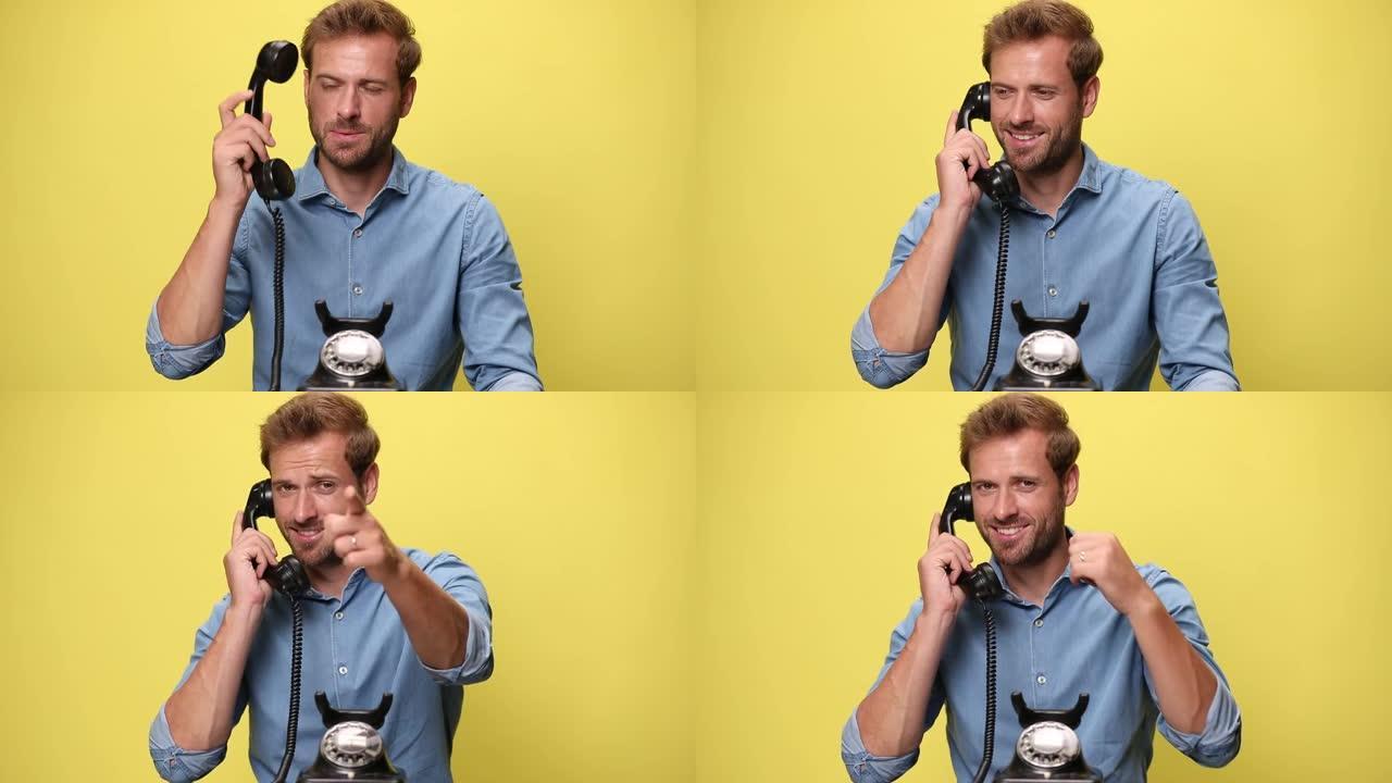 快乐的商人在旧电话上聊天，指着相机，在黄色背景上给我打电话。