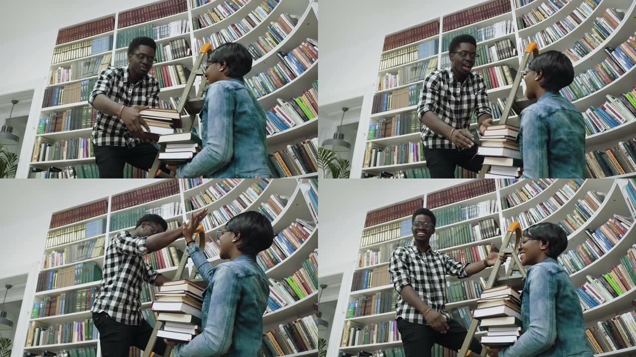非洲男人站在梯子上向大学图书馆的非洲女孩赠书时从书架上选书的底视图