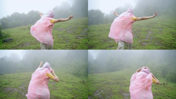 穿着粉色雨衣的年轻亚洲女性徒步旅行者的慢动作后视，在山中刮起大风，在雨中徒步旅行。漂亮女孩在美丽的大