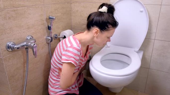 患病的年轻女子在厕所里呕吐，坐在家里的地板上，出现食物中毒的症状。