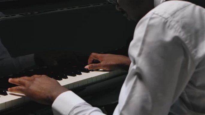 一个非裔美国人用双手在三角钢琴上演奏柔和的古典音乐。音乐家的双手以慢动作关闭