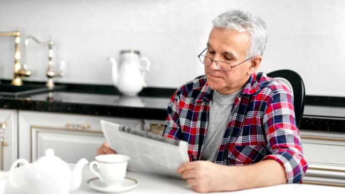 戴眼镜的老年家庭男人在厨房吃早餐时看报纸