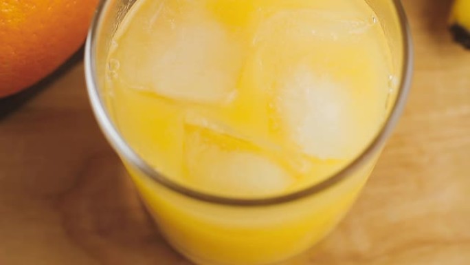 全杯有机橙汁和冰块放在木制桌子上，极端特写