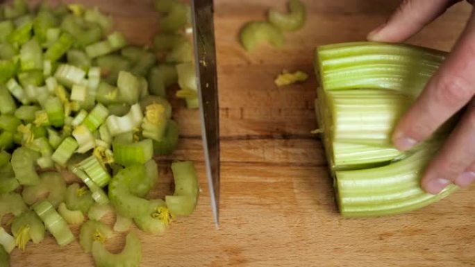 在木制切割表面的餐厅厨房里用刀切碎芹菜。厨师切芹菜在厨房做饭。手在砧木板上用刀切片芹菜背景。慢动作。