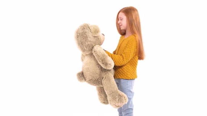 美丽的小女孩的特写肖像，美丽的红头发微笑着，拿着一个大熊玩具。孤立，在白色背景上。快乐的童年概念。真