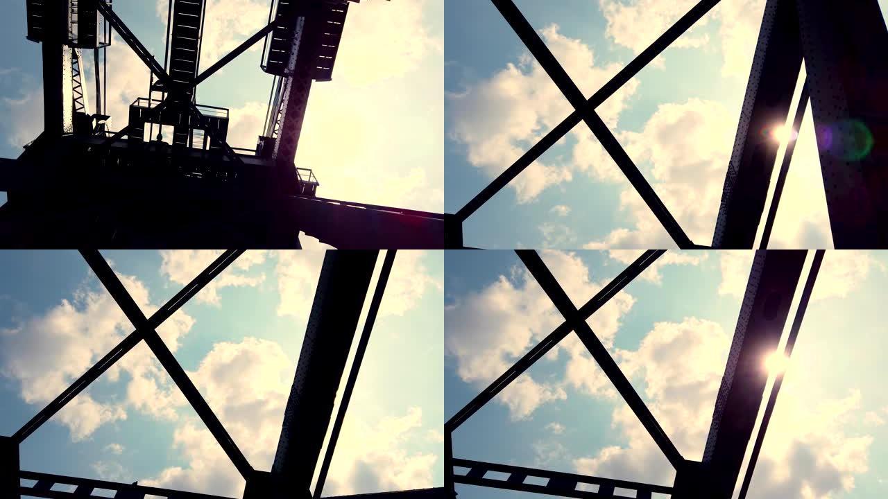 从运动中的车窗观看。一座铁制零件的大桥，映照着蔚蓝的多云天空和灿烂的阳光。金属桥逆天