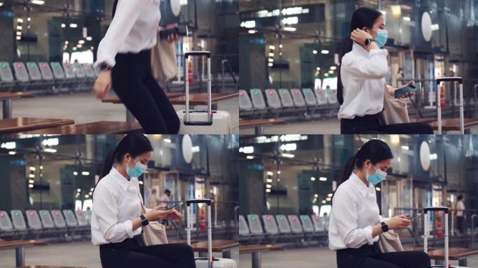 美丽的女性戴着外科口罩保护，并在机场航站楼外坐在椅子上使用智能手机，并在新型冠状病毒肺炎大流行期间保