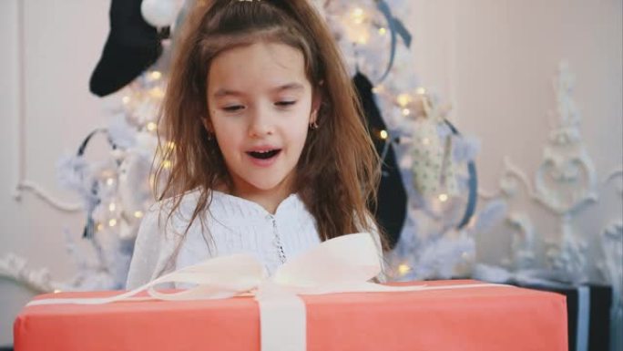 特写新年延时视频，一个孩子从礼品盒后面出现，嘴巴张开，揉着手，准备打开礼物。
