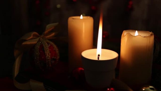 圣诞心情: 三根点燃的蜡烛，一根在前景中有大火焰，红色和金色的球，剪纸球，缎面金丝带，在弱光下拍摄的