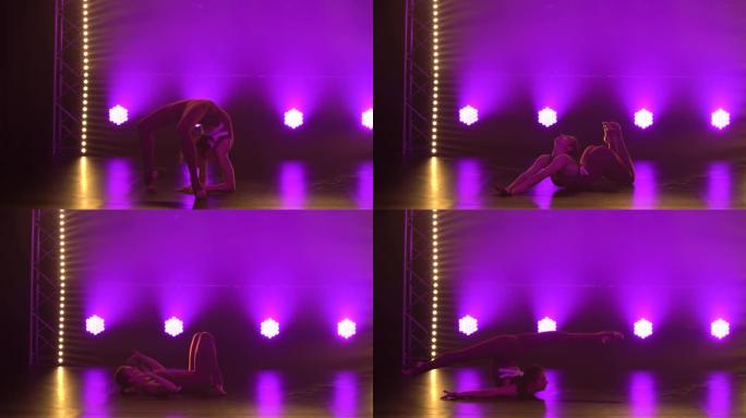 灵活的专业女运动员表演艺术体操的复杂杂技元素。在带有霓虹灯的黑暗工作室拍摄。剪影。特写