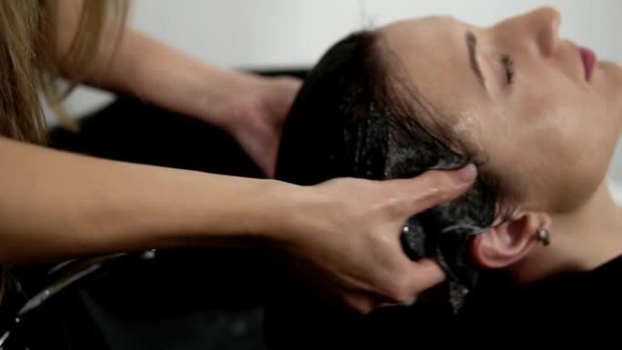 理发师在理发前洗长发女人，并将洗发水按摩到头皮上。理发师的手洗头，使洗发水在头上起泡。特写