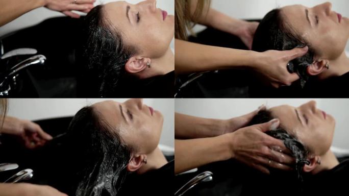 理发师在理发前洗长发女人，并将洗发水按摩到头皮上。理发师的手洗头，使洗发水在头上起泡。特写