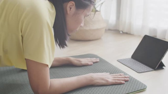 亚洲女性在瑜伽垫上做铺板后练习，早上在家平板电脑上在线训练