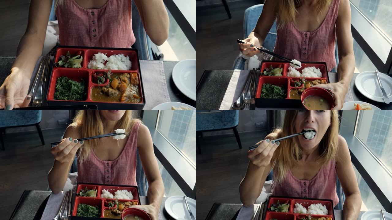 年轻女子在餐馆吃日本菜。女性吃便当牛传统日本食物