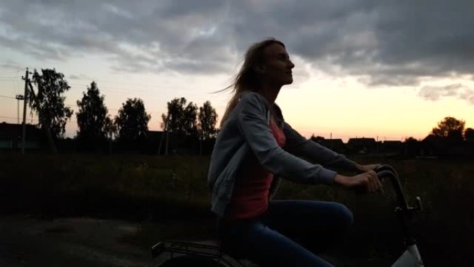 日落时分，金发女郎在草地上骑自行车。农村