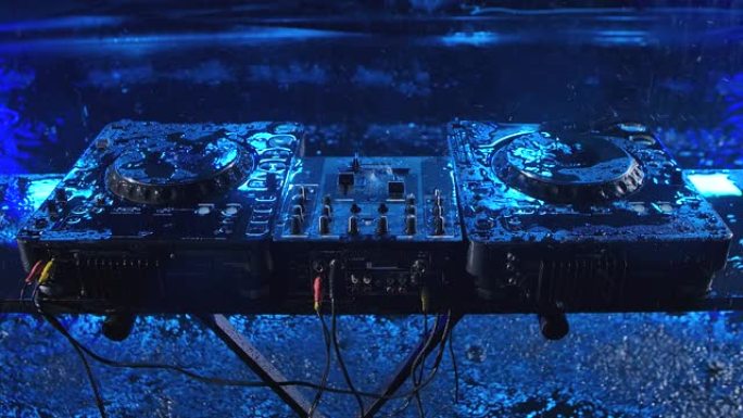 音频混合控制器站在带有蓝色照明的黑暗工作室中。DJ工具在倾盆大雨中。顶视图。特写。慢动作