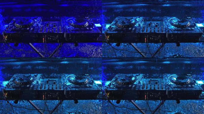 音频混合控制器站在带有蓝色照明的黑暗工作室中。DJ工具在倾盆大雨中。顶视图。特写。慢动作