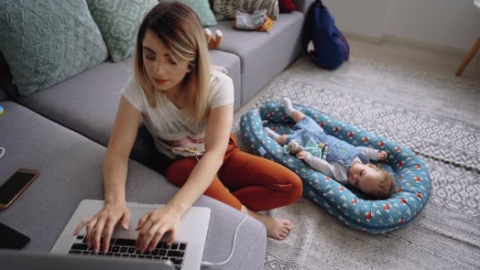 年轻的单身母亲在家工作，男婴躺在她旁边