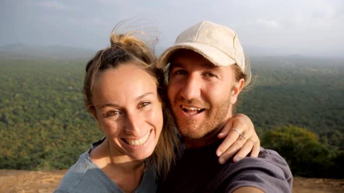 开朗的夫妇在岩石上自拍，俯瞰锡吉里亚著名的寺庙和周围绿色郁郁葱葱的丛林。人们在网上分享自拍，一起旅行