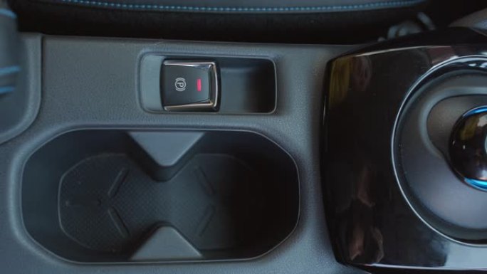 手指按下停车系统的按钮。现代汽车内部细节的特写镜头。电动汽车中的驻车制动按钮