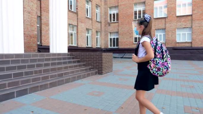 在户外，戴着防护面具和盾牌，背着背包的女学生在校园里上学。covid19爆发后重返学校