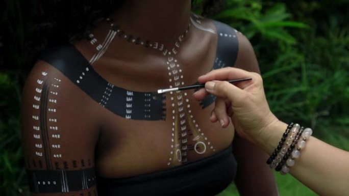 坐在热带花园里的非洲女孩化妆并在身体上画了民族线条