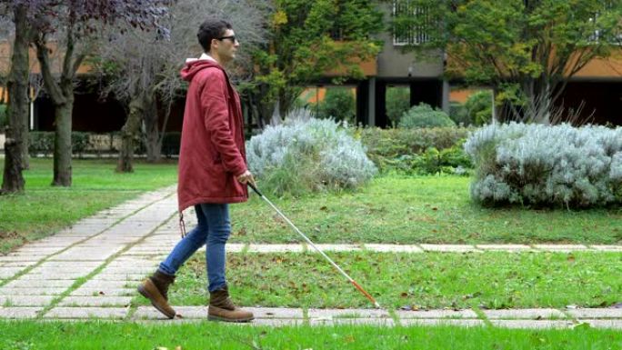 障碍、自主indipendence。在城市公园里拄着拐杖走路的盲人年轻人