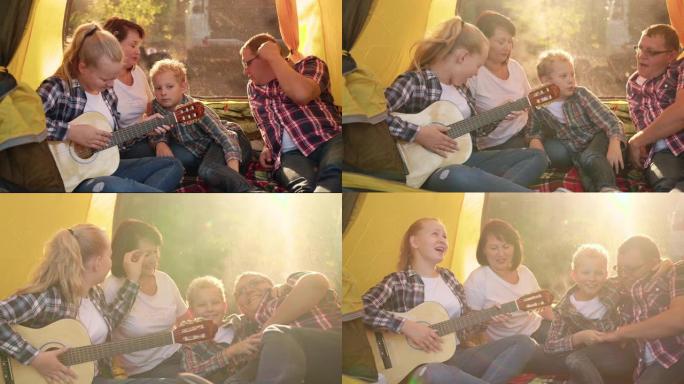 旅游家庭在森林徒步旅行的野营帐篷里用吉他唱歌。友好的家庭在阳光背景下的露营唱歌。十几岁的女孩为家人弹