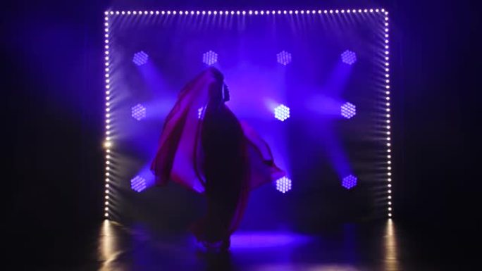 剪影一个穿着红色纱丽的年轻女孩舞者。印度民间舞蹈。在带有烟雾和蓝色霓虹灯的黑暗工作室中拍摄。慢动作
