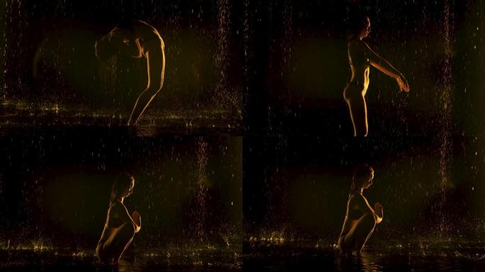 年轻女子在雨中在黑暗的工作室里练习瑜伽体式。黑色背景和黄色霓虹灯。水滴中身体的轮廓。慢动作