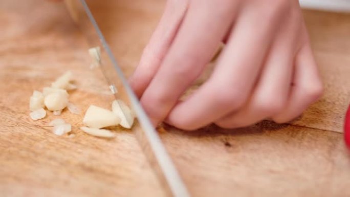 用厨师刀在4k中近距离切碎大蒜。在慢动作的切菜板上切割/切片大蒜的概念。