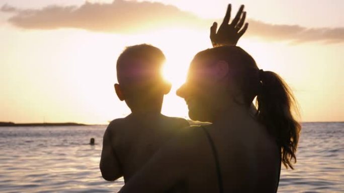 妈妈和宝宝在海水中游泳的剪影他们向太阳日落挥手告别