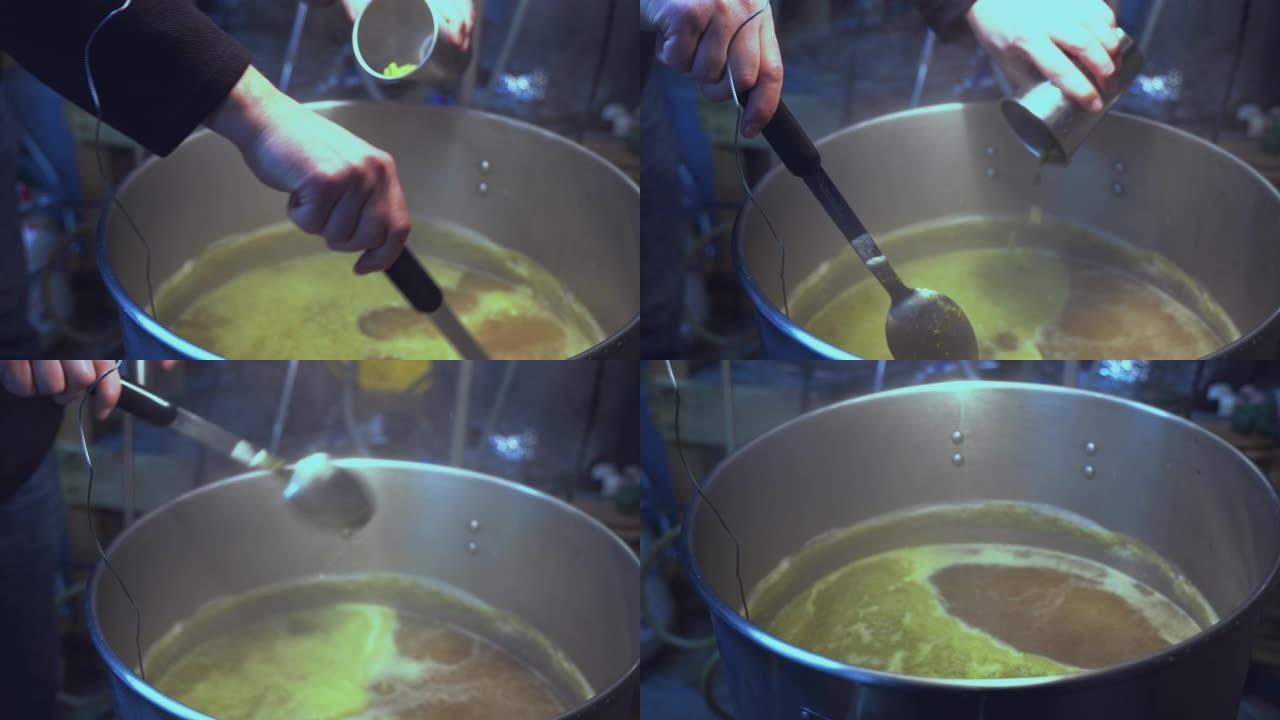 在小型地下室家庭啤酒厂自制酿造。一个人正在向麦芽汁中添加原料，麦芽汁在大锅中沸腾。