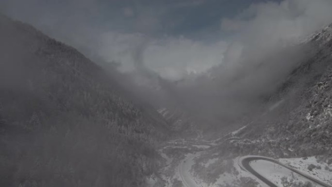 无人机在高海拔的山谷中穿越云层，下方有一条小路