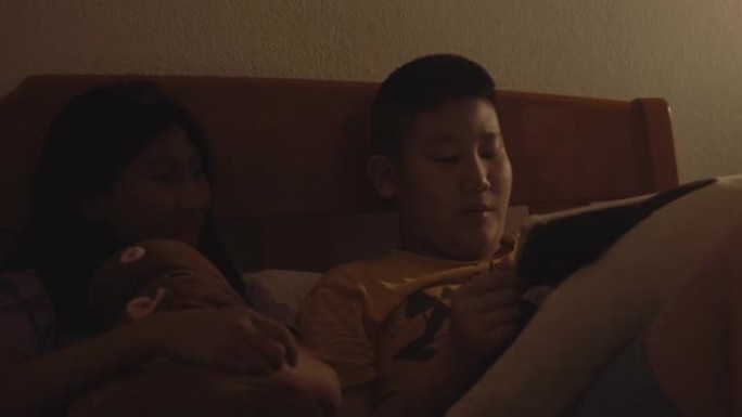 亚洲男孩和女孩晚上一起在床上用数字平板电脑看电影。