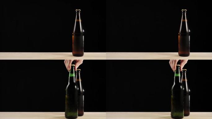 新鲜啤酒。手将一个绿色的瓶子和美味的工艺啤酒放在棕色瓶子和啤酒在黑色背景下的木制桌子上。水滴冷新鲜啤