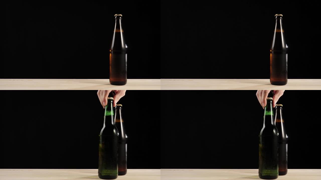 新鲜啤酒。手将一个绿色的瓶子和美味的工艺啤酒放在棕色瓶子和啤酒在黑色背景下的木制桌子上。水滴冷新鲜啤